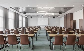 a large conference room with rows of chairs arranged in a semicircle , and a projector on the wall at Courtyard Basel