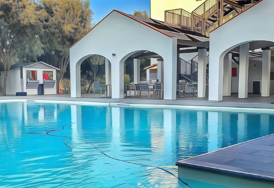 a large , well - maintained swimming pool with a white building and wooden decking , surrounded by lush greenery at Smy Civico Zero