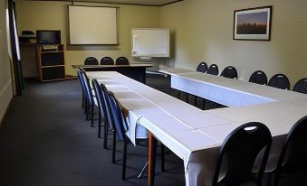 a long dining table with white tablecloths and black chairs in a room with a projector screen at Lyndoch Hill