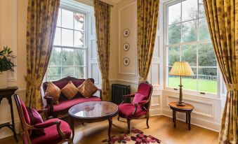 a cozy living room with red furniture , a rug on the floor , and large windows at Doxford Hall Hotel and Spa