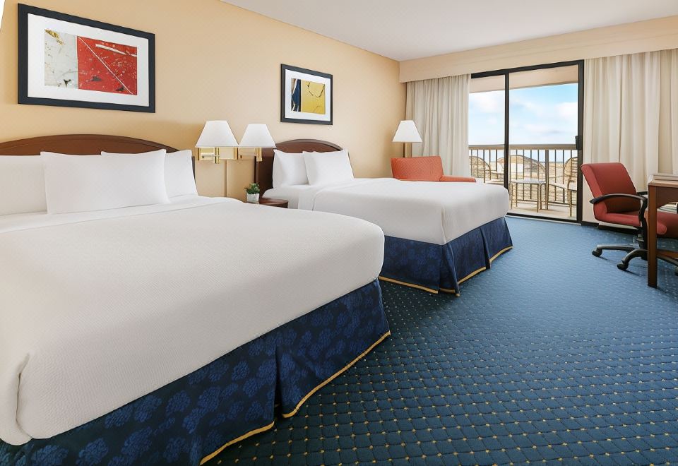 a hotel room with two beds , each made up with white linens and blue carpet , next to a window with a view of the city at Courtyard Flint Grand Blanc
