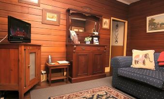 a cozy living room with wooden walls , a couch , a chair , and a tv . a dresser in the room at Westbury Gingerbread Cottages