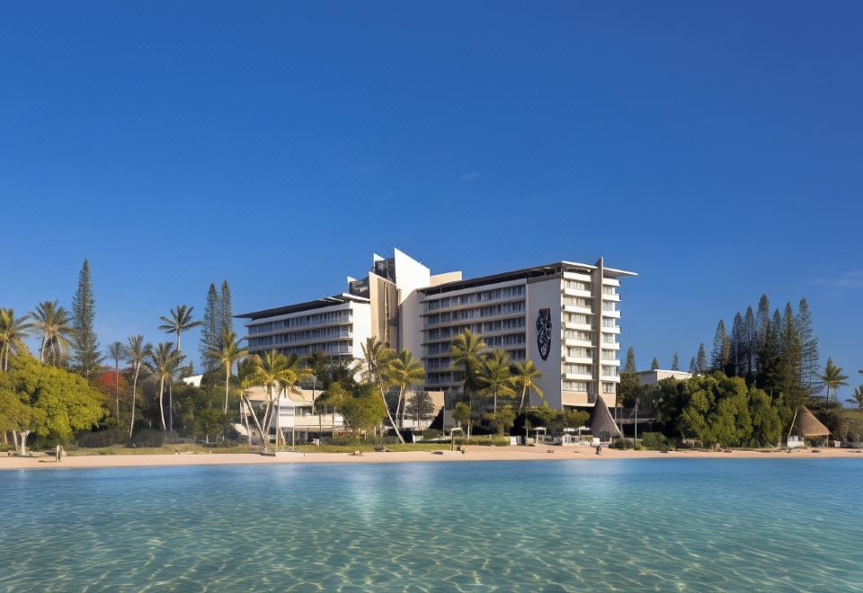 a large hotel surrounded by palm trees and a body of water , creating a picturesque setting at Chateau Royal Beach Resort & Spa, Noumea