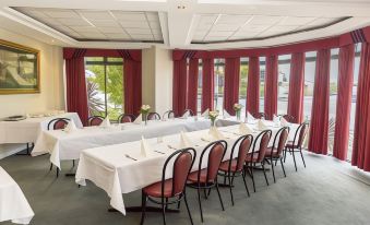 a large dining room with several tables set for a meal , surrounded by red curtains and a window at Barkly Motorlodge