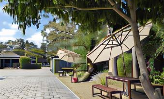 a paved walkway with several benches , umbrellas , and trees lining the path , creating a serene outdoor environment at The Balnarring Motel