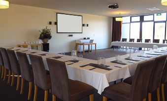 a conference room set up for a meeting , with chairs arranged in rows and a projector on the wall at Barwon Heads Resort