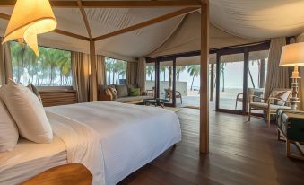 a large bed with white linens is in a room with wooden floors and walls , overlooking the ocean at Karpaha Sands