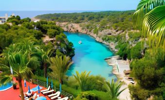 a beautiful tropical landscape with clear blue water , white cliffs , and lush green trees , as well as sun loungers and umbrellas scattered throughout the at Aparthotel Ona Cala Pi Club