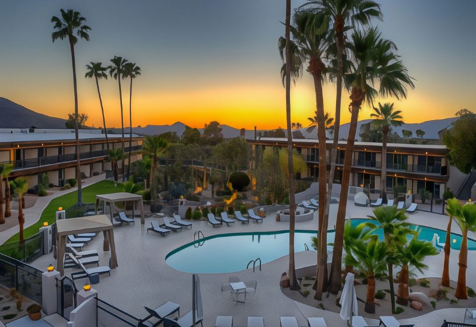 a large swimming pool surrounded by palm trees , with the sun setting in the background at Civana Wellness Resort & Spa