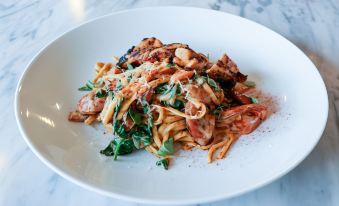 a white plate with a delicious pasta dish , topped with meat and vegetables , sitting on a dining table at St. James Hotel Selma, Tapestry Collection by Hilton