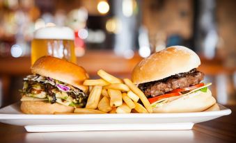 a plate of food with two hamburgers and french fries , along with a glass of beer at Nightcap at Westside Hotel