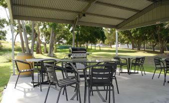 a patio area with a dining table and chairs under a covered structure , surrounded by trees at Fern Bay Motel