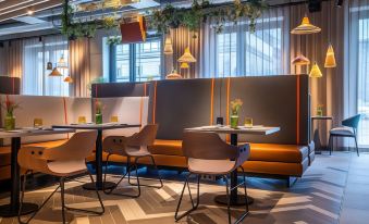 a modern restaurant with orange and brown seating , pendant lights , and greenery on the walls at Hilton Garden Inn Mannheim