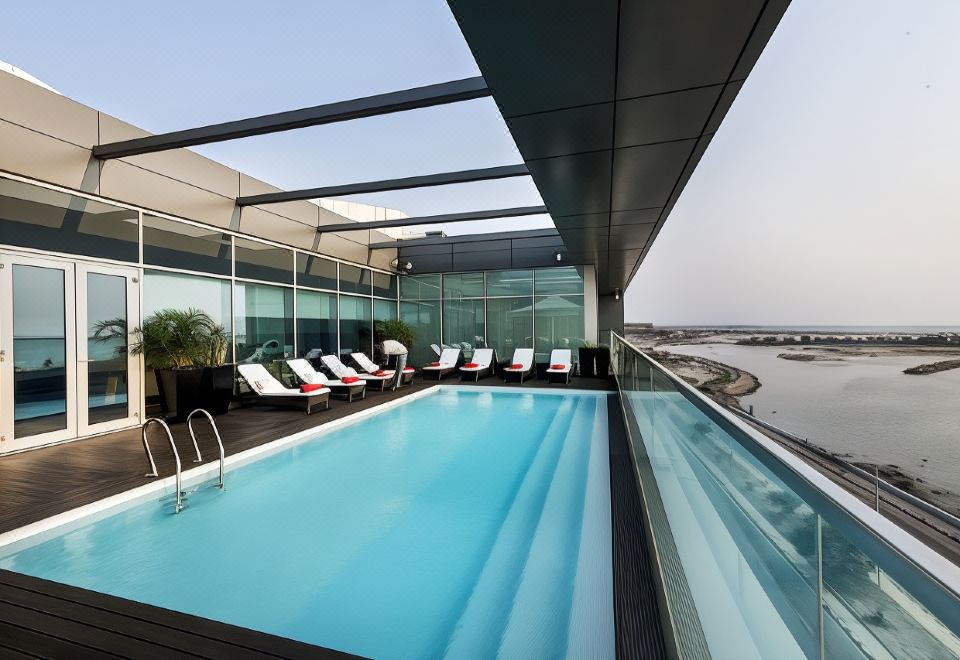 a large swimming pool is surrounded by lounge chairs and a balcony with a view of the ocean at Hotel Baia