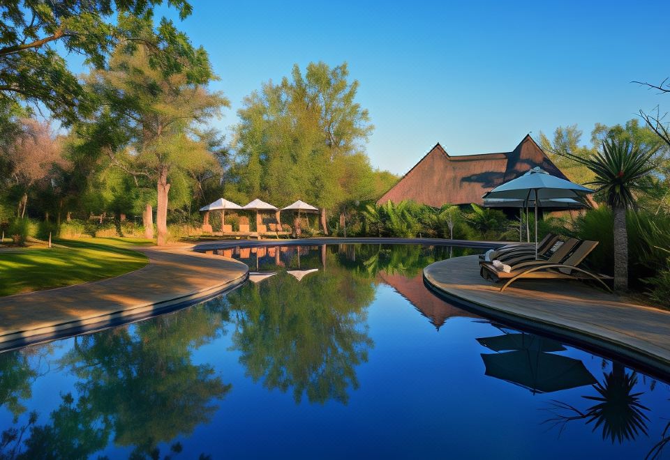 a large outdoor pool surrounded by grass , with several lounge chairs and umbrellas placed around it at Mokuti Etosha