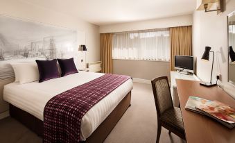 a modern hotel room with a bed , tv , and desk , along with a view of the city through large windows at Mercure Swansea Hotel
