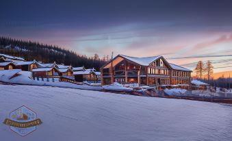 a snow - covered ski resort with a large lodge in the foreground , surrounded by trees and mountains in the background at Mountain Lodge