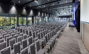 an empty conference room with rows of gray chairs and a projector screen at the front at Hotel Grand Chancellor Brisbane