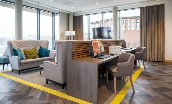 a modern office space with wooden furniture , large windows , and yellow flooring , as well as comfortable seating arrangements at Hampton by Hilton Stockton on Tees