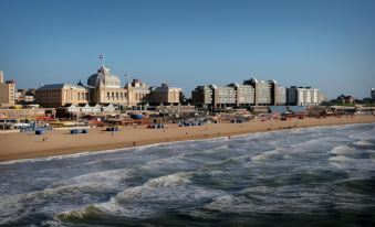 a city beach with many people enjoying the sun , sand , and water , as well as a large building in the background at The Collector