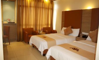 a hotel room with two beds , each made up with white sheets and brown pillows , next to a window with gold curtains at Grand Pasundan Convention Hotel