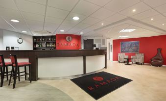 a hotel lobby with a reception desk , chairs , and a rug featuring the ramada logo at Days Inn by Wyndham London Stansted Airport