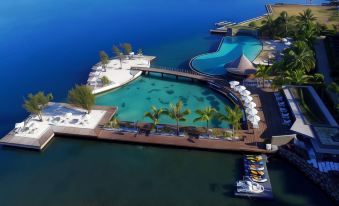 a large , circular pool with a walkway leading to it is surrounded by palm trees and lounge chairs at Te Moana Tahiti Resort