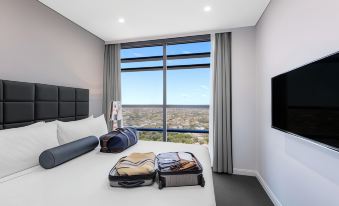 a modern bedroom with a large window overlooking a cityscape , and two suitcases placed on the bed at Meriton Suites North Sydney