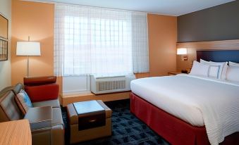 a hotel room with a large bed , a couch , and a window with curtains , all set against an orange wall at TownePlace Suites Grand Rapids Airport