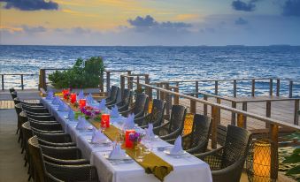 a long dining table set up on a deck overlooking the ocean , with multiple chairs arranged around it at Dusit Thani Maldives