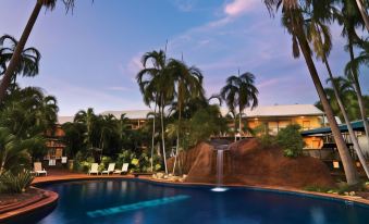 a large swimming pool with a waterfall and palm trees in front of a hotel at Travelodge Resort Darwin