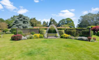 a lush green lawn with a metal arched structure in the middle , surrounded by trees and bushes at Best Western Priory Hotel