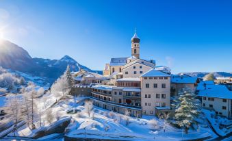 a large building with a tower is surrounded by snow and trees , with mountains in the background at Romantik Hotel Turm