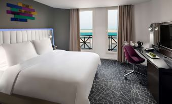 a modern bedroom with a large window offering a view of the ocean , white bed , and purple chair at Park Inn by Radisson Dammam