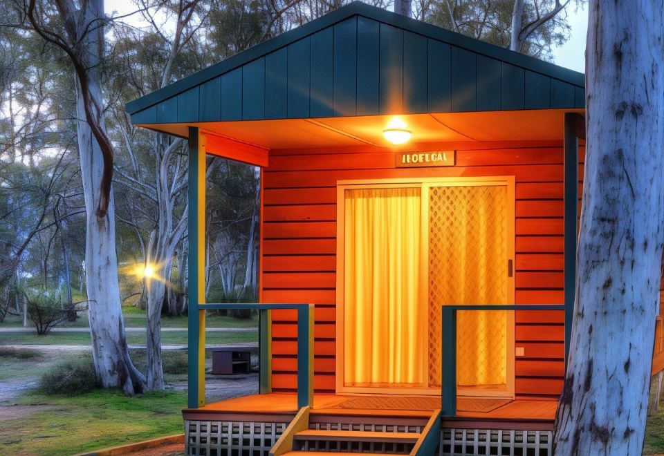 a small wooden cabin in a park , surrounded by trees and lit up at night at Kosciuszko Tourist Park