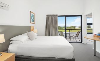 a large bed with white linens is in a room with a sliding glass door leading to a balcony at Corrigans Cove
