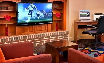 a living room with a tv , couch , coffee table , and two red chairs , as well as a soccer player on the television at Residence Inn Cranbury South Brunswick