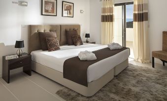 a large bed with a brown headboard and white linens is in a room with a window at Belmar Spa & Beach Resort
