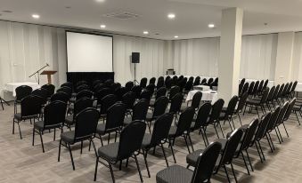 a conference room with rows of black chairs arranged in a semicircle , and a projector screen mounted on the wall at Burnie Central Townhouse Hotel