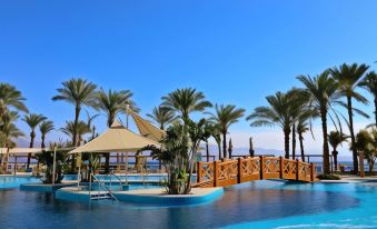 a large swimming pool with palm trees and a covered area is surrounded by a wooden deck at Steigenberger Hotel & Nelson Village, Taba