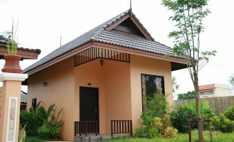 a small , beige - colored house with a black door and a balcony , surrounded by green grass and trees at Chalicha Resort