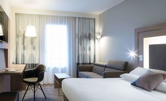 a modern hotel room with a white bed , couch , and dining table , all decorated in light colors at Novotel Chateau de Versailles