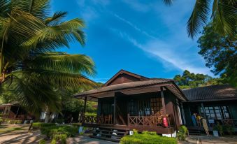 a wooden house with a brown roof is surrounded by palm trees and has a sign on the porch at Perhentian Island Resort