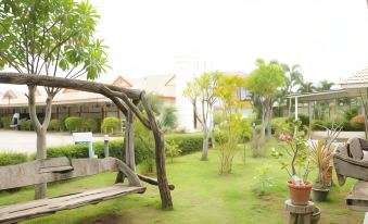 a lush green lawn with a wooden swing hanging from a tree , surrounded by trees and plants at Saraburi Garden Resort