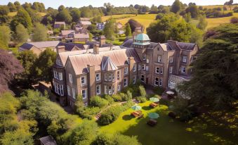 aerial view of a large mansion surrounded by a lush green garden , with trees and grass in the foreground at Makeney Hall Hotel