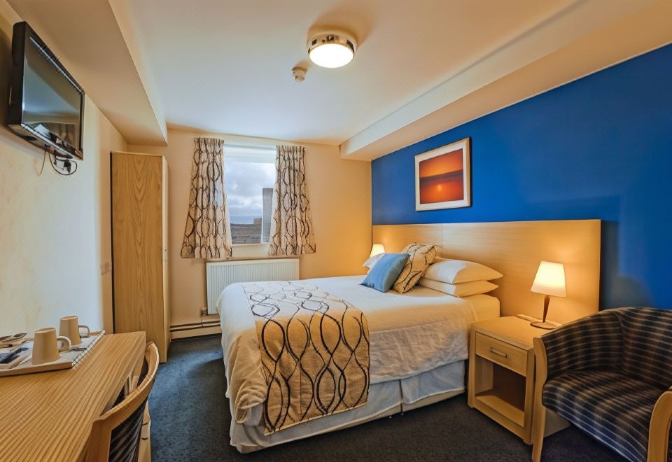 a well - arranged hotel room with a large bed , curtains , and other amenities , along with a desk and nightstand at Royal Maritime Hotel