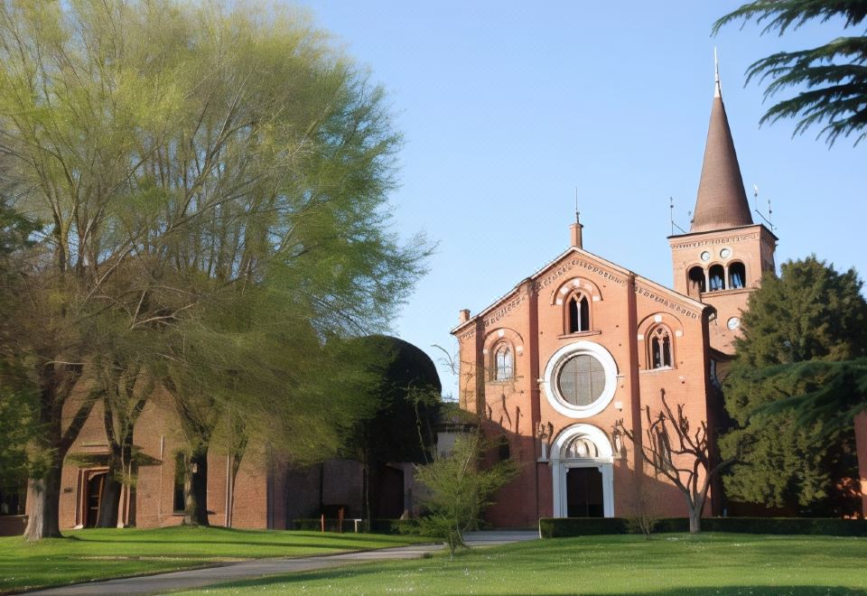 a brick church with a tall spire and a curved window is surrounded by trees and grass at Hotel Majestic