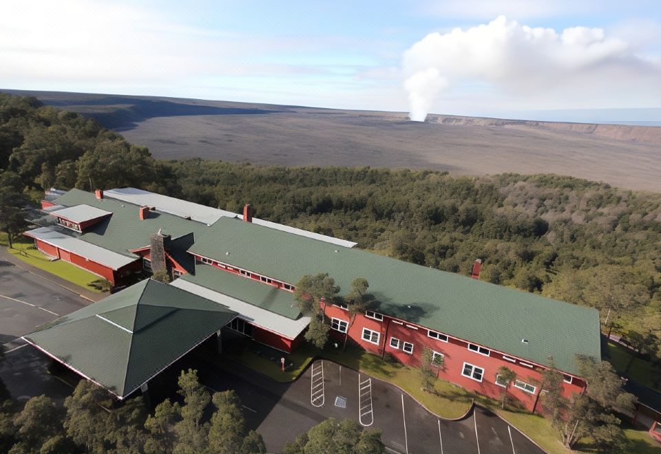 aerial view of a large red building with a green roof , surrounded by trees and a lake in the background at Volcano House