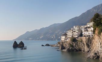 a picturesque coastal town is perched on a cliff overlooking the ocean , with mountains in the background at Hotel la Lucertola