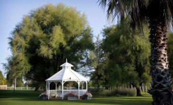 a white gazebo is situated in a grassy area with trees and bushes surrounding it at Parklands Resort Mudgee